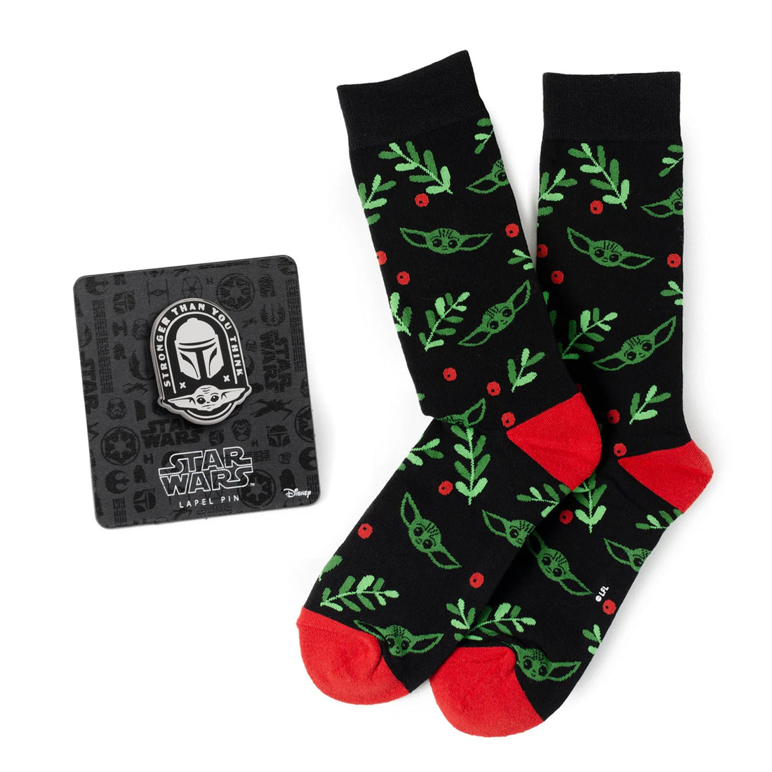 A pair of black holiday-themed crew socks with Grogu, green sprigs, and red berries, next to a Star Wars Mandalorian enamel lapel pin.