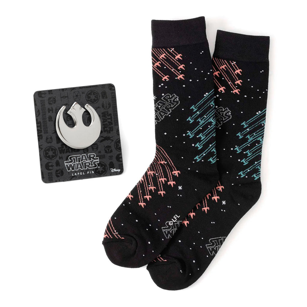 A pair of black Star Wars themed crew socks with an X-Wing and TIE fighter battle pattern next to a silver Rebel Alliance symbol lapel pin.