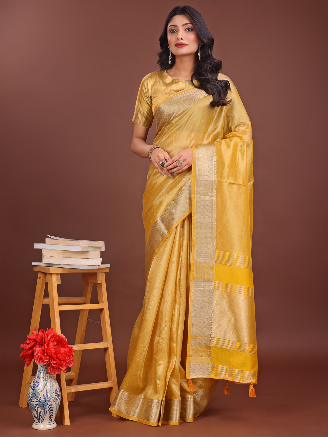 Yellow organza saree with a rich golden zari border and decorative pallu tassels.