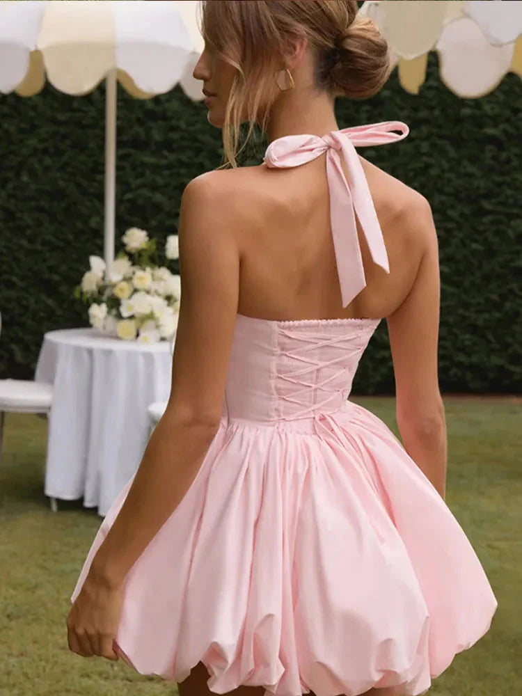 Model wearing a pink corset-style mini dress with a voluminous puffball hem and halter neck tie
