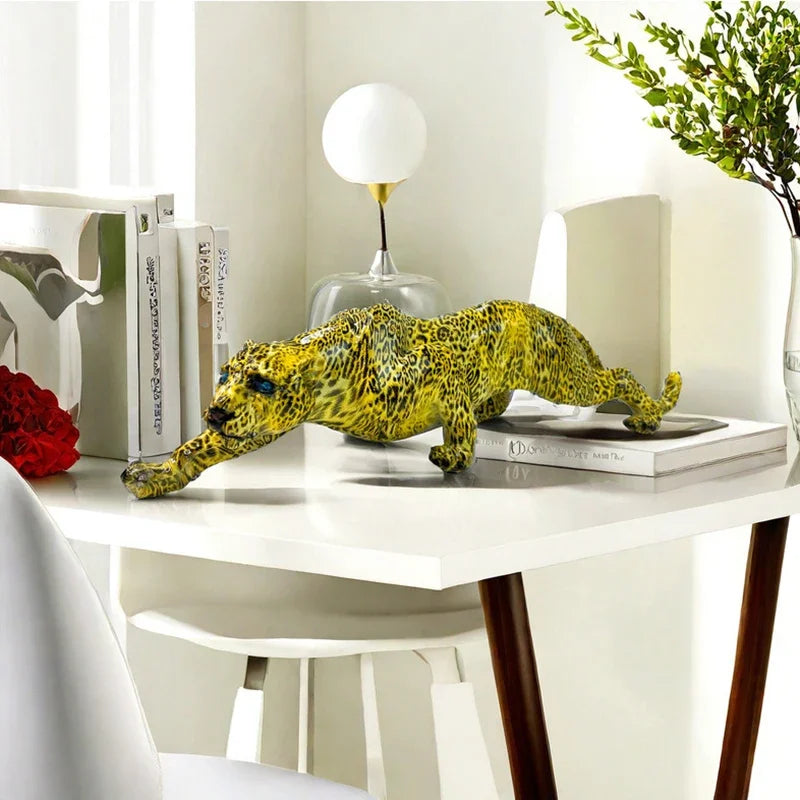 A detailed yellow resin leopard sculpture displayed on a white desk next to books and a lamp.