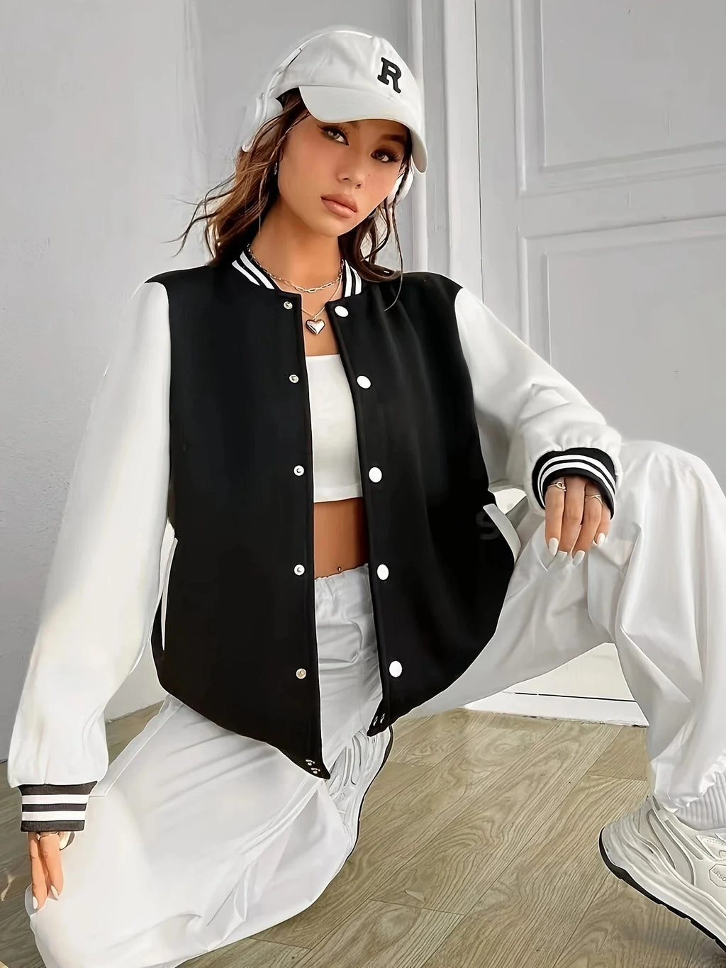 A woman wearing a black and white colorblock oversize varsity baseball jacket with button closure