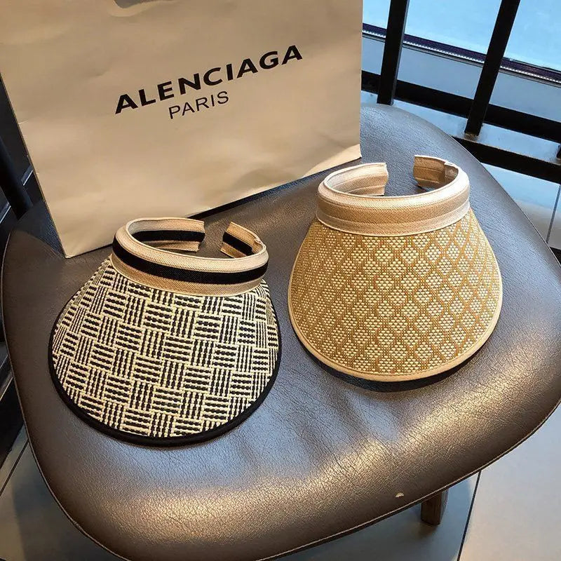 A selection of woven straw sun visors displayed on a chair with a designer shopping bag in the background.