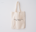 Keep Your Eyes On Jesus canvas market tote in beige with black text, shown on a neutral background.