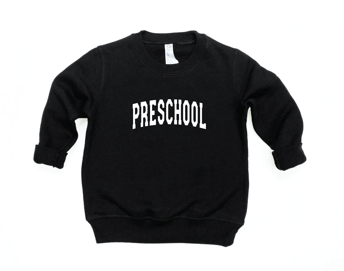 Child wearing a black and white preschool varsity pullover in a casual knit fabric.