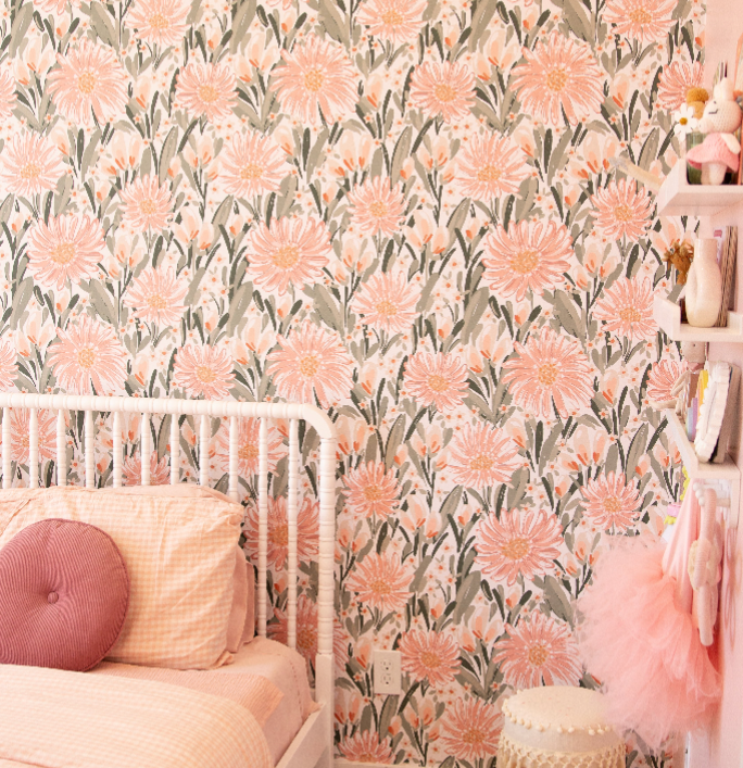 Auden floral wallpaper in peach and sage-green with a bohemian aesthetic on a clean bedroom wall.