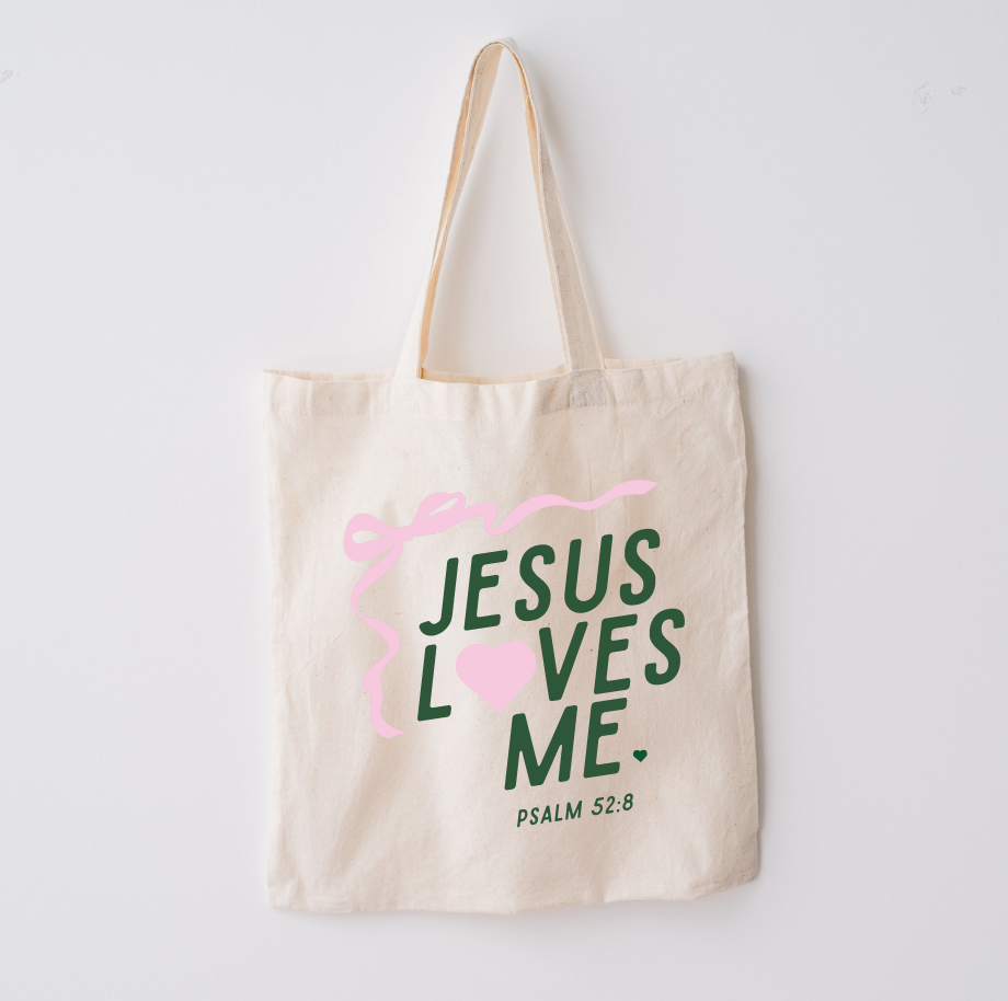 Natural beige cotton market tote with forest green text reading Jesus Loves Me and light pink graphic accents