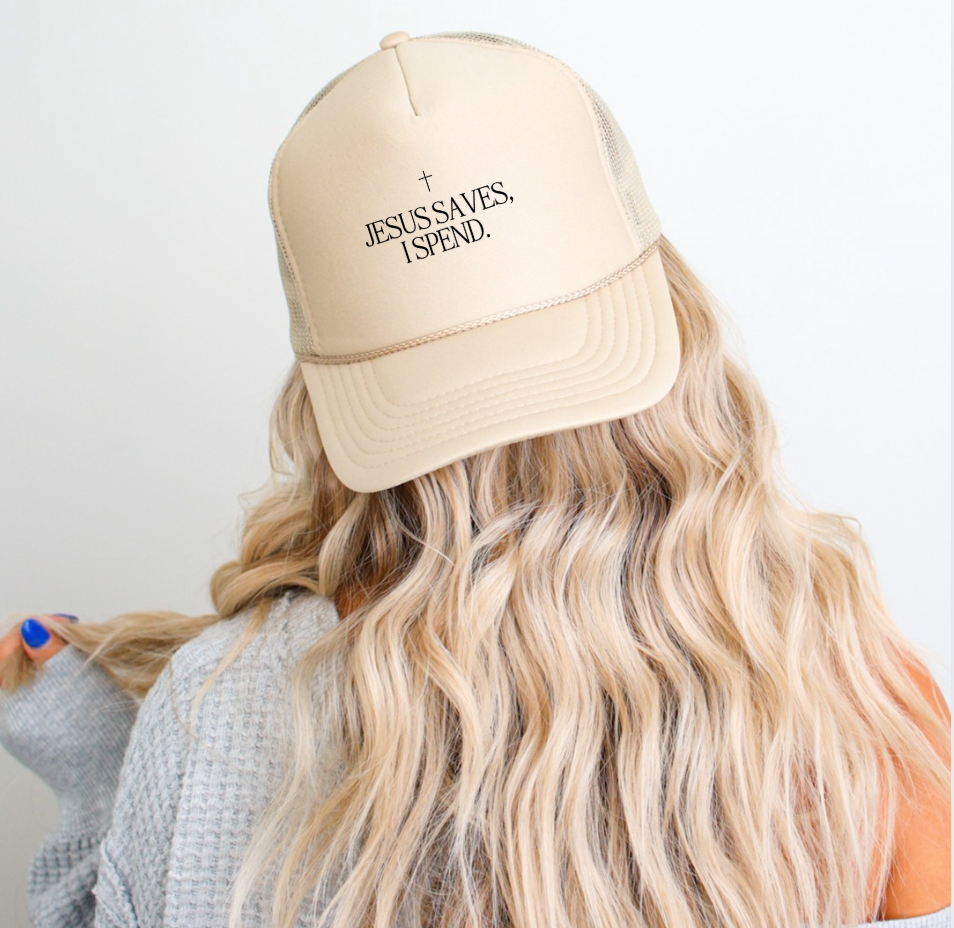 Neutral beige Jesus Saves, I Spend trucker hat with snap-back closure, styled for a casual streetwear look.
