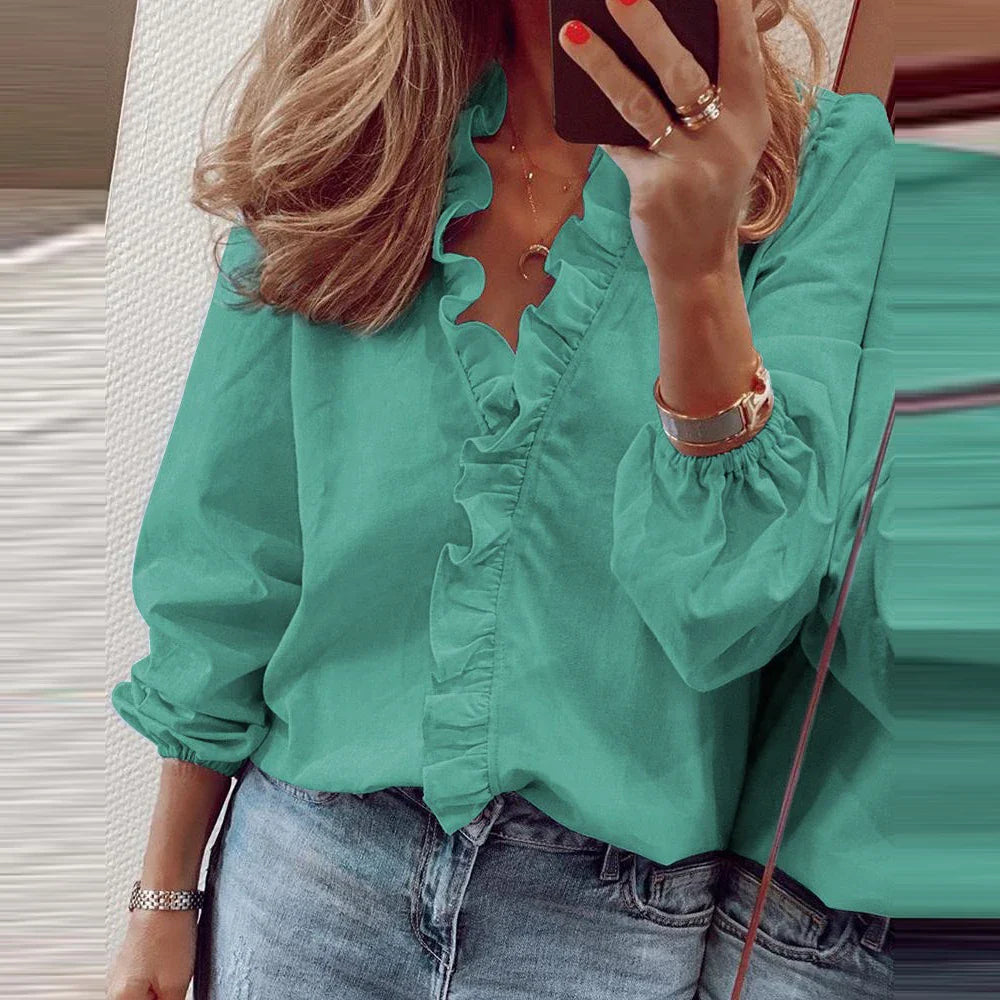 A woman wearing a long-sleeved ruffled V-neck blouse in teal or white, styled with blue jeans.