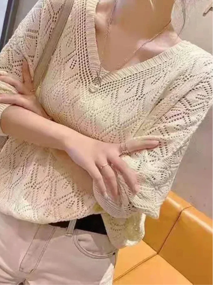 A woman wearing a beige v-neck hollow-knit crochet sweater with long sleeves.