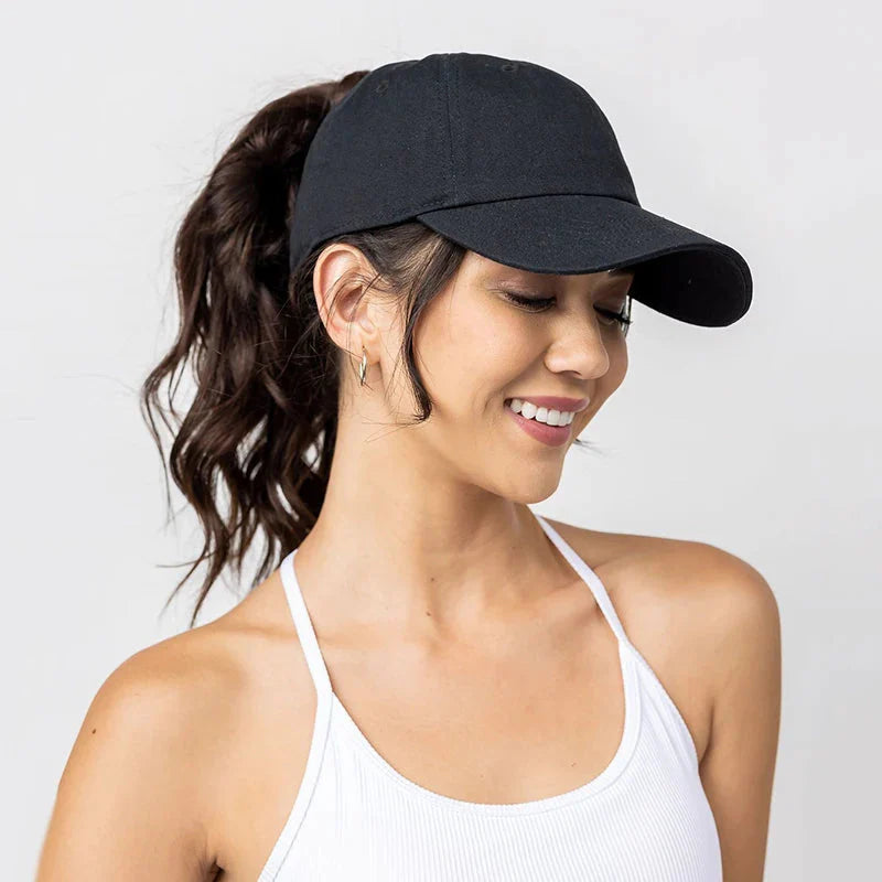 A woman wearing a black high-ponytail baseball cap with a messy bun hairstyle, viewed from the side.