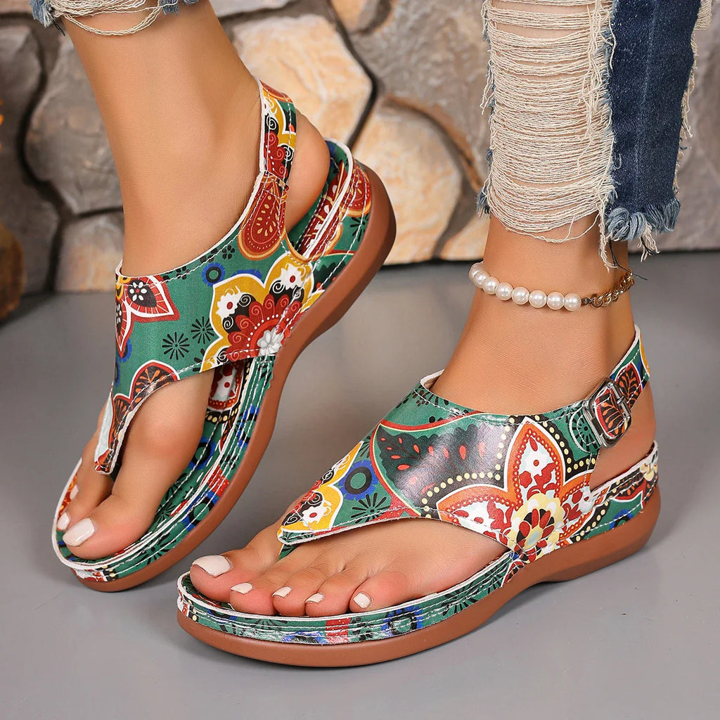 Close-up view of women wearing colorful floral print wedge thong sandals with ankle buckle straps.