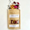 A kraft paper pouch labeled Serenade Simmer Pot Kit surrounded by dried lavender, red rose petals, and orange slices on a white surface.
