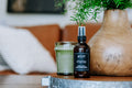 Amber glass bottle of Shiplap air and room spray sitting on a wooden surface next to a plant.