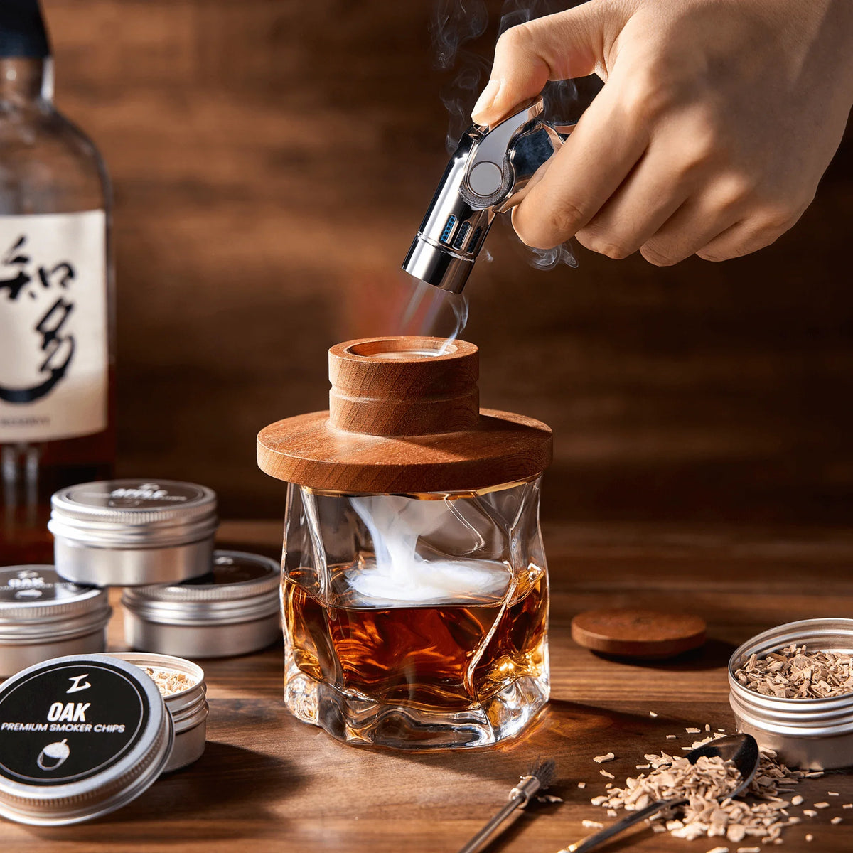 Modern crystal whisky glass smoker kit with torch and wood chips on a bar surface