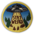 Circular Stay Weird patch featuring a retro UFO flying saucer and a bright yellow tractor beam