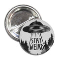 Round monochromatic black and white Stay Weird button pin on a plain background