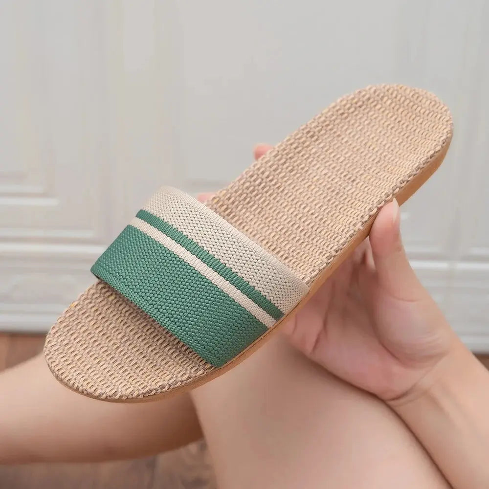 A pair of women's flat summer slippers with a green and neutral striped fabric strap and a textured hemp-style footbed.