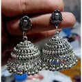 A pair of lightweight oxidized silver jhumka earrings decorated with white pearls on a neutral background.