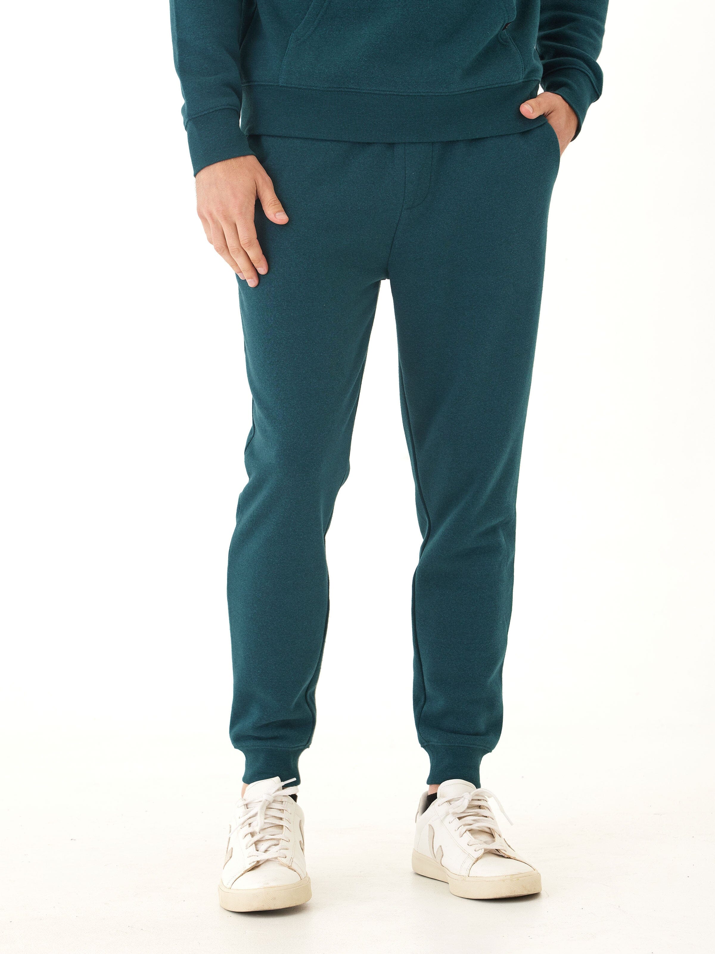 Men wearing slim fit triblend fleece joggers in teal heathered knit, styled with a minimalist athleisure aesthetic.