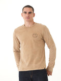 Man wearing a mineral wash tan and brown graphic long sleeve tee with volcan-style side tab branding