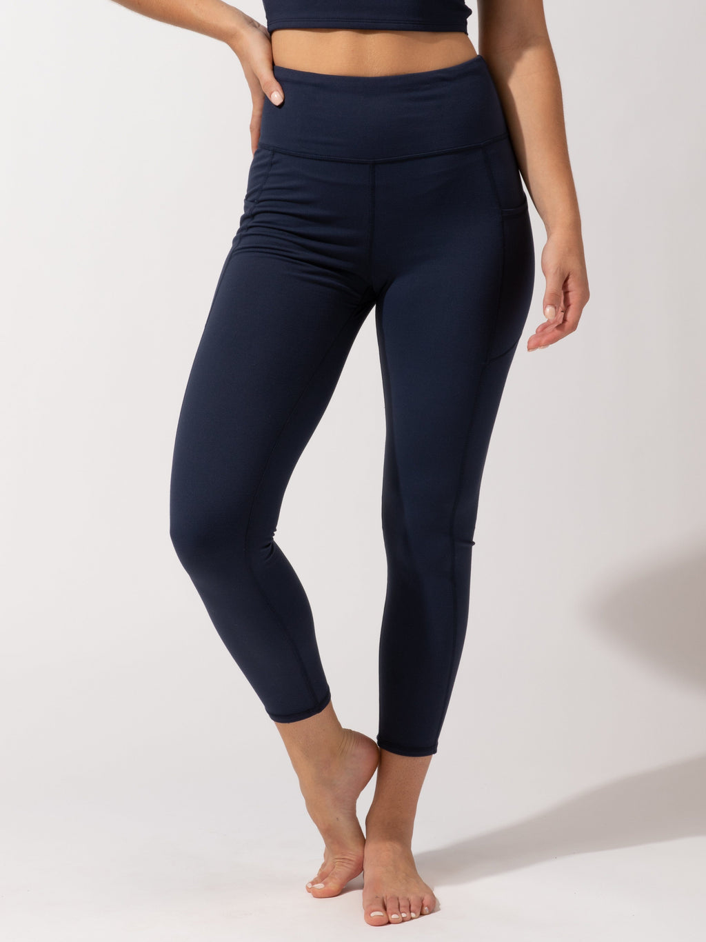 A pair of solid navy blue high-rise ankle-length leggings with side pockets, shown in a sporty, minimalist style.