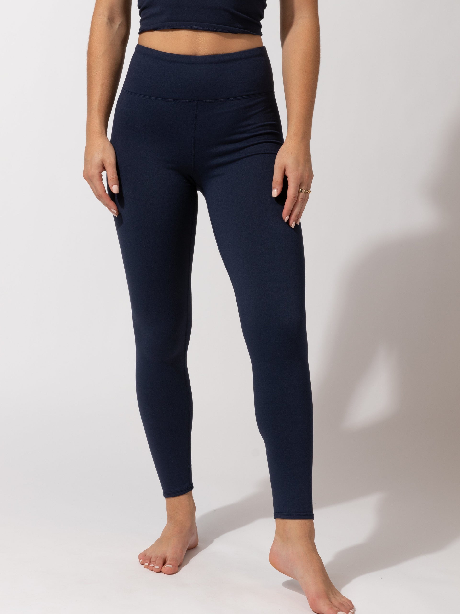 Women wearing solid navy blue full length high-rise leggings for an athletic minimalist look.
