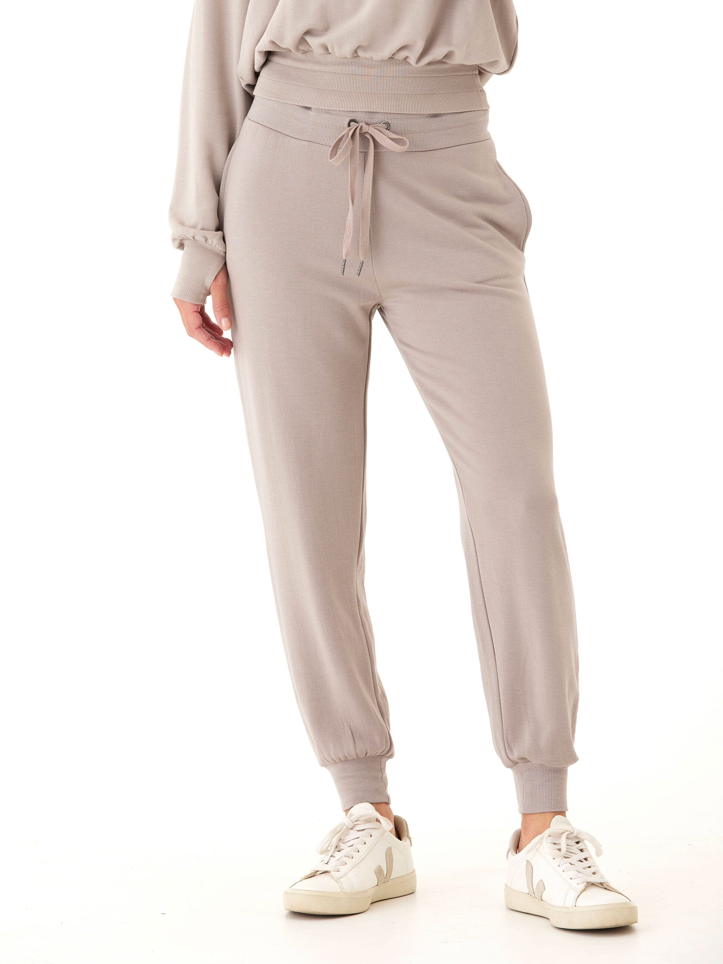 Woman wearing high-rise Core Feather Fleece Joggers in neutral taupe with ribbed ankle cuffs.