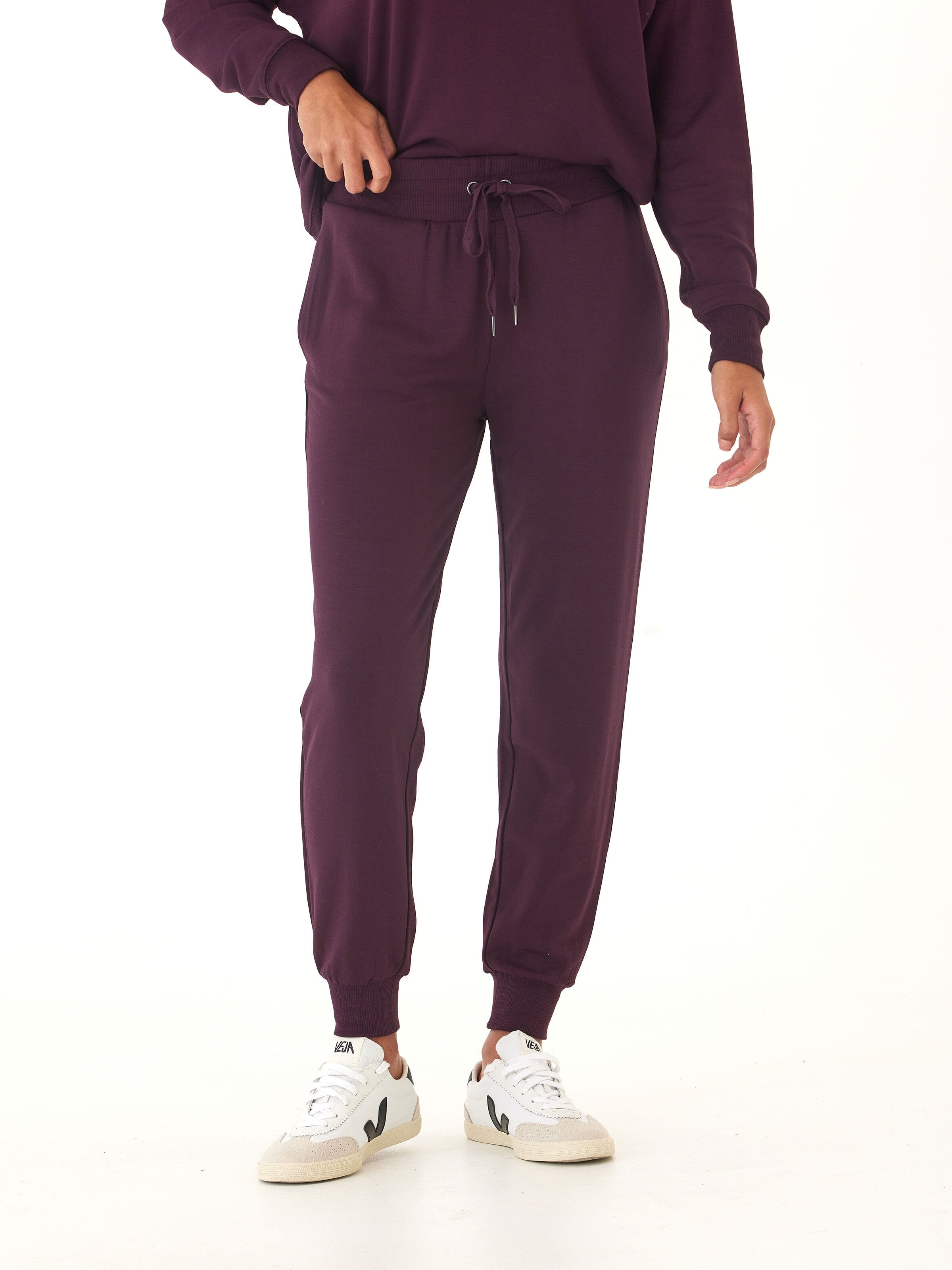 A woman wearing relaxed fit dark purple Core Feather Fleece Joggers with a drawstring waist and ribbed cuffs.