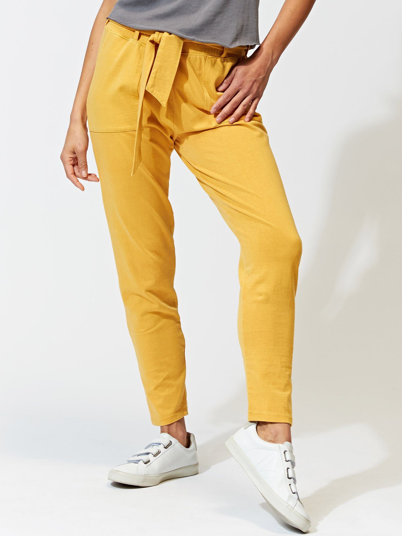 Mustard yellow organic cotton joggers with a tie front, patch pockets, and tapered ankle, worn in a casual loungewear setting.