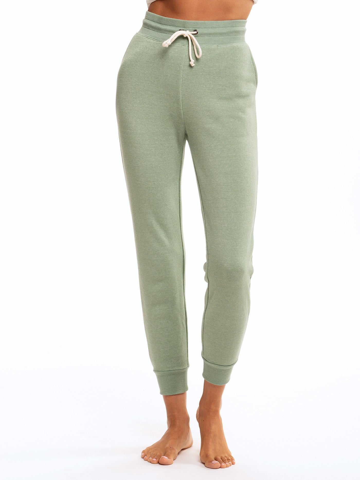Woman wearing sage green slim fit triblend joggers with a drawstring waist and tapered ankle cuffs.