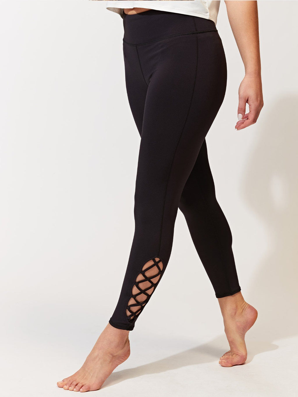 Model wearing black high-waisted 7/8 leggings with lace-up ankle detail in a sporty athleisure setting.
