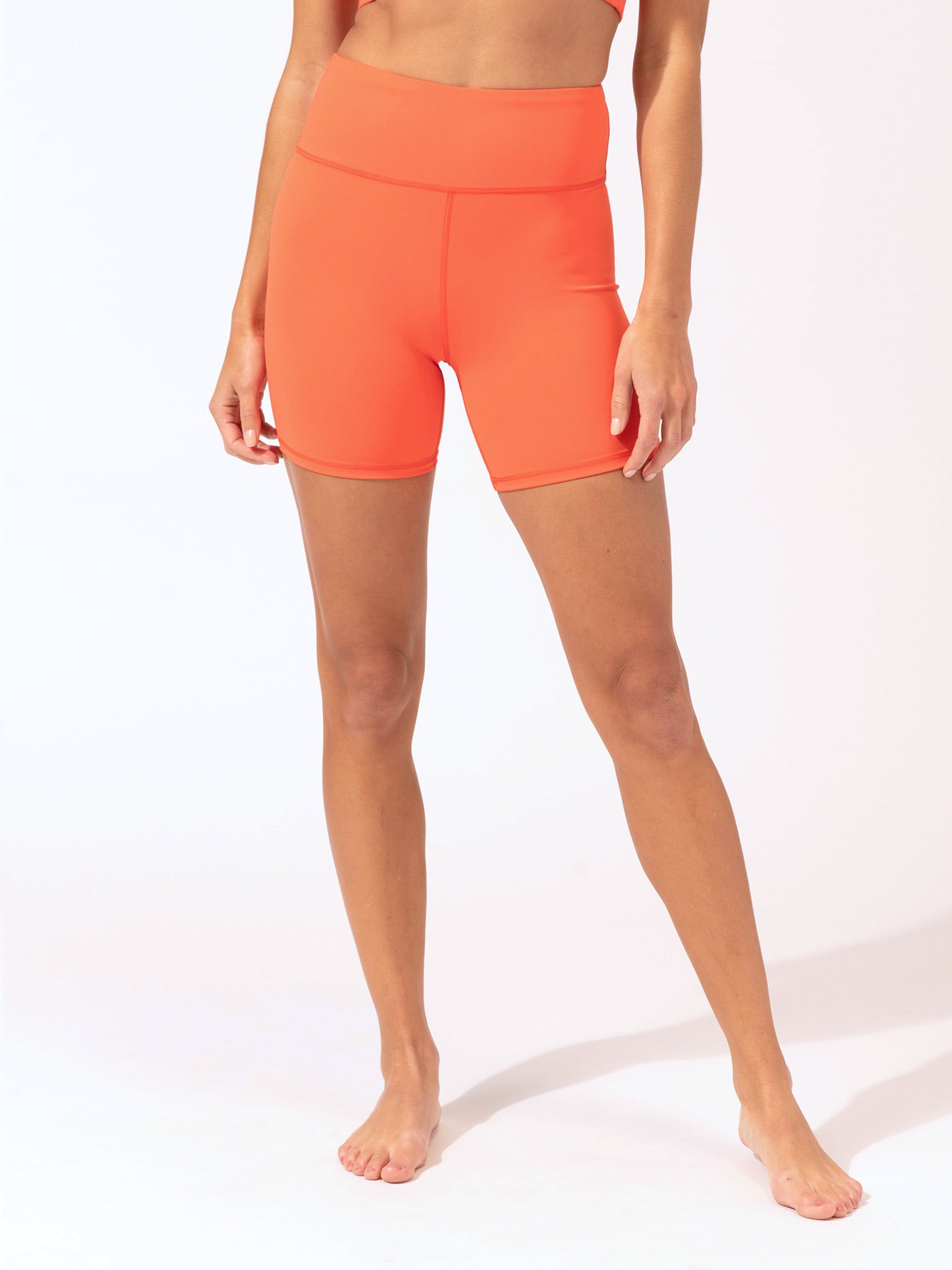 Woman wearing orange high-rise Sylvana active shorts in a sporty, minimalist style.