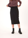 A woman wearing a fitted black Marla Luxe Jersey midi skirt with a pull-on waistband in a minimalist setting.