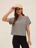 Woman wearing a grey relaxed-fit short sleeve crew neck t-shirt with a chest pocket, minimalist athleisure style.