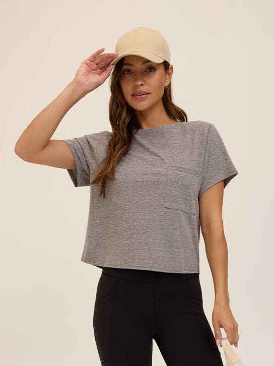 Woman wearing a grey relaxed-fit short sleeve crew neck t-shirt with a chest pocket, minimalist athleisure style.