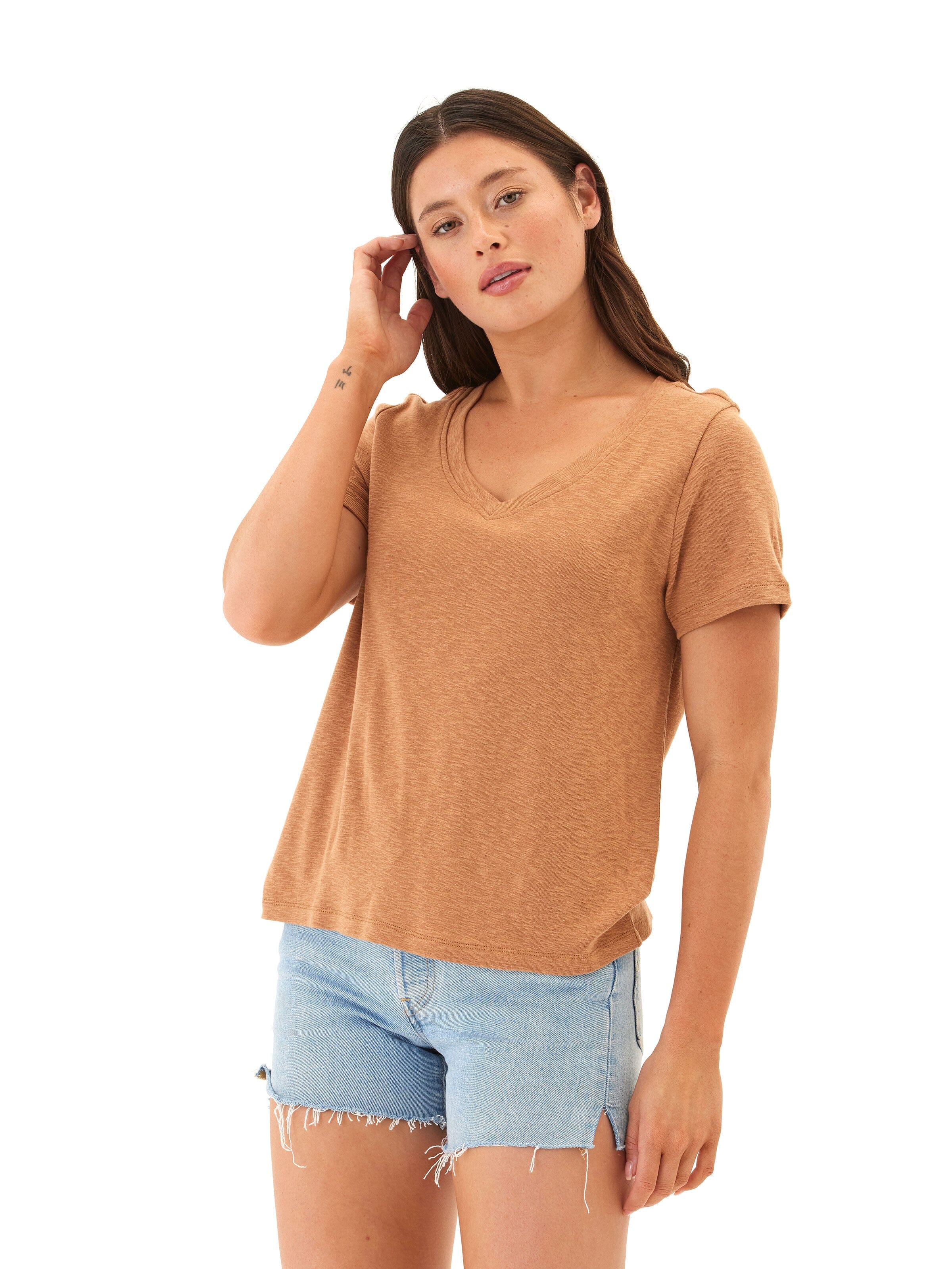 A woman wearing a tan minimalist slub jersey V-neck top with gathered back detail.