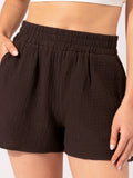 Woman wearing relaxed fit dark brown high-rise organic cotton gauze shorts in a bohemian loungewear style.