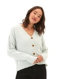A woman wearing a soft mint-green boucle knit cardigan with a V-neckline and button-front closure in a cozy, minimalist setting.