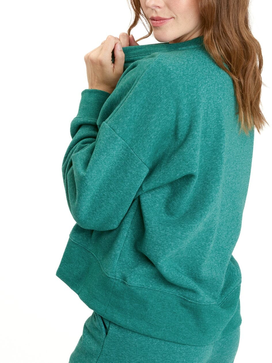 Woman wearing a solid green Naia Triblend Fleece Pullover in a minimalist loungewear style