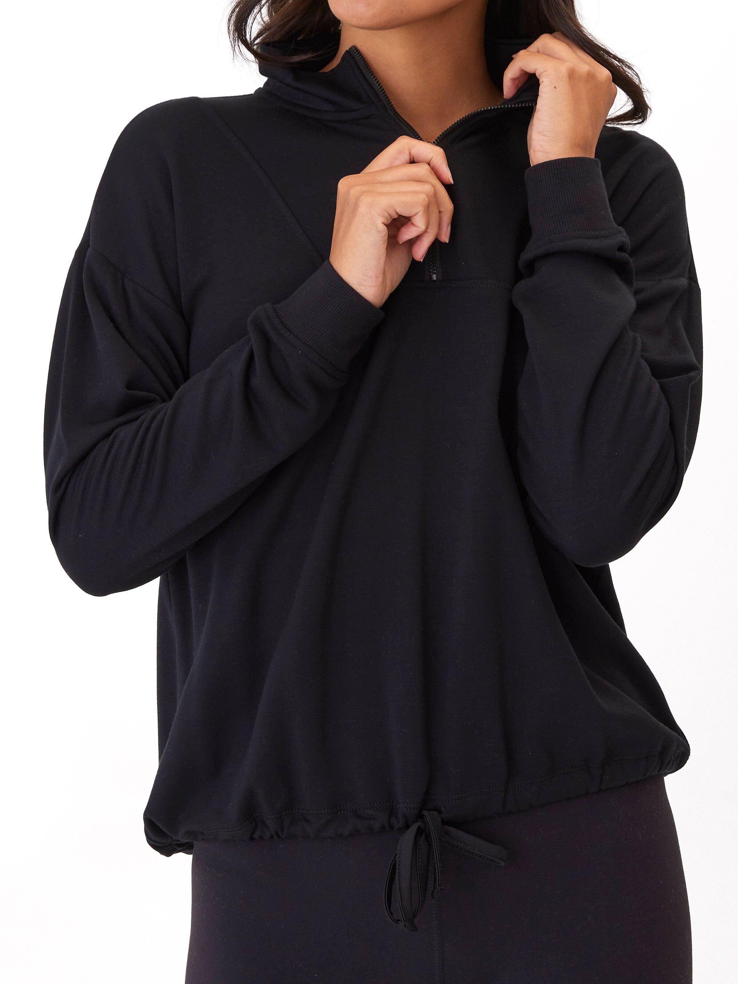 A woman wearing a solid black Nyla Feather Fleece Half Zip Pullover with a collared neckline and drawstring hem.