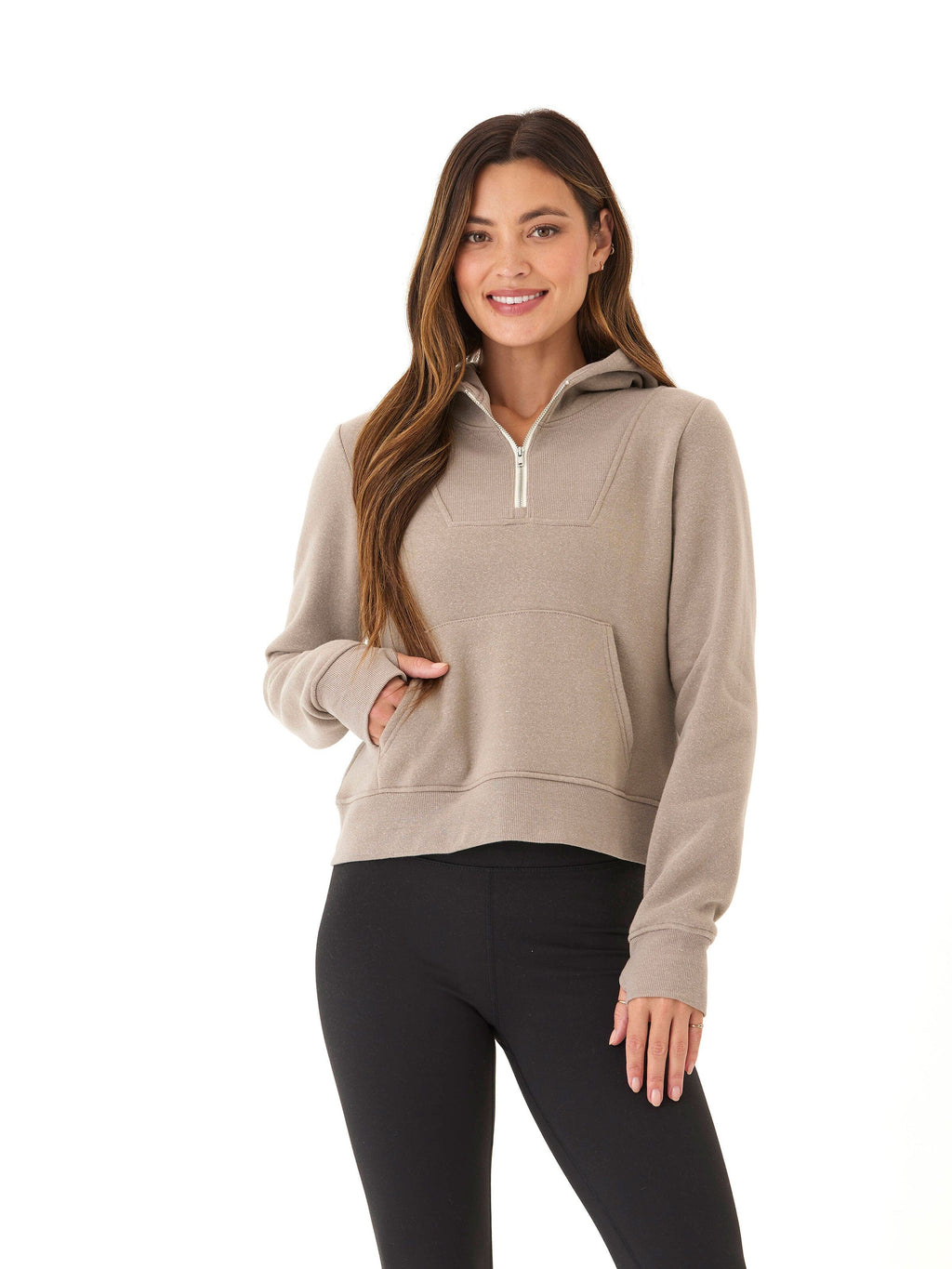 Model wearing a Tyra Triblend Fleece Quarter Zip Hoodie in taupe with thumbholes and pockets visible.