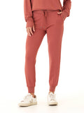 Women wearing rust-colored Feather Fleece jogger pants with a tapered fit and ribbed cuffs in a minimalist setting.