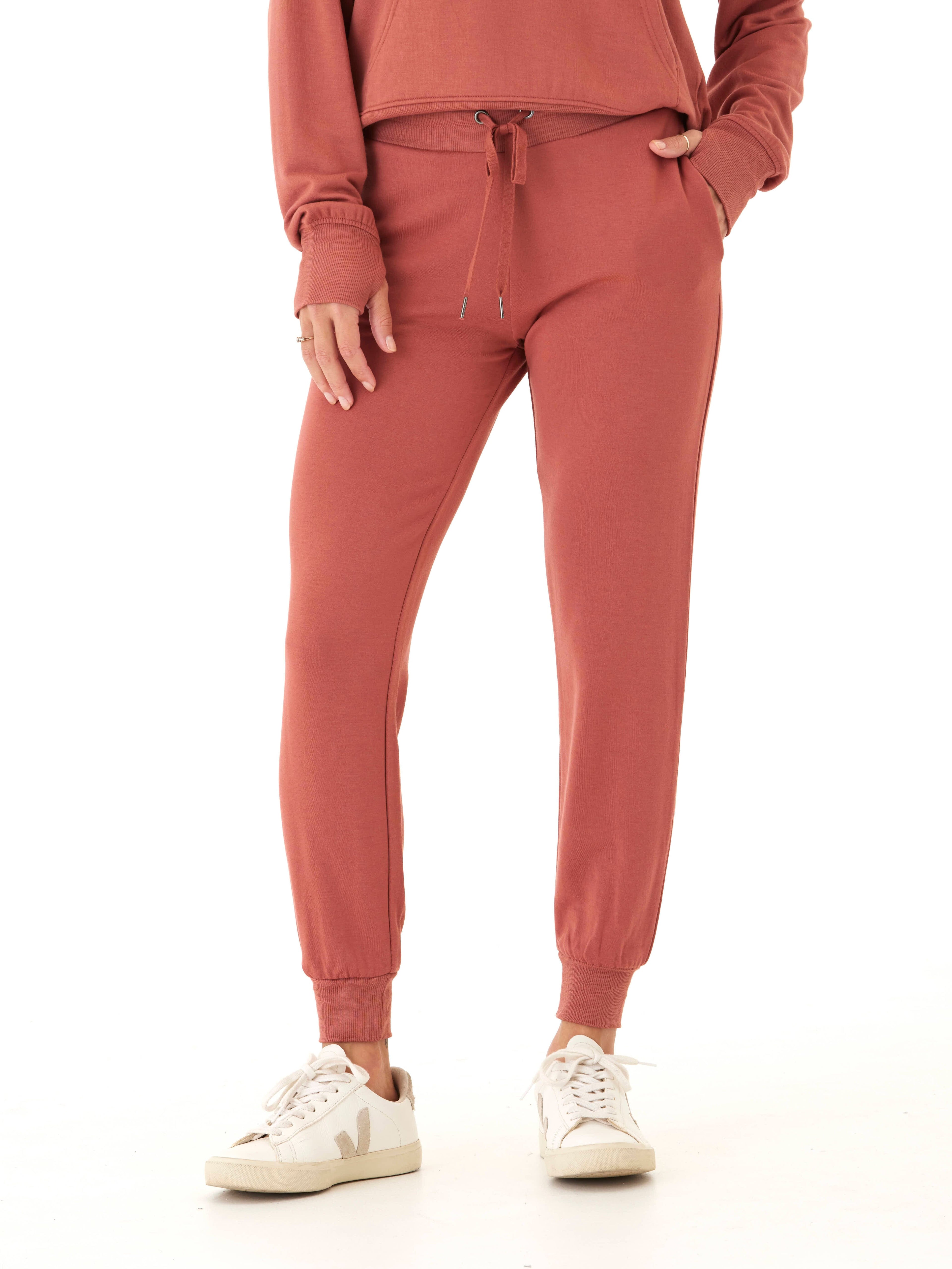 Women wearing rust-colored Feather Fleece jogger pants with a tapered fit and ribbed cuffs in a minimalist setting.