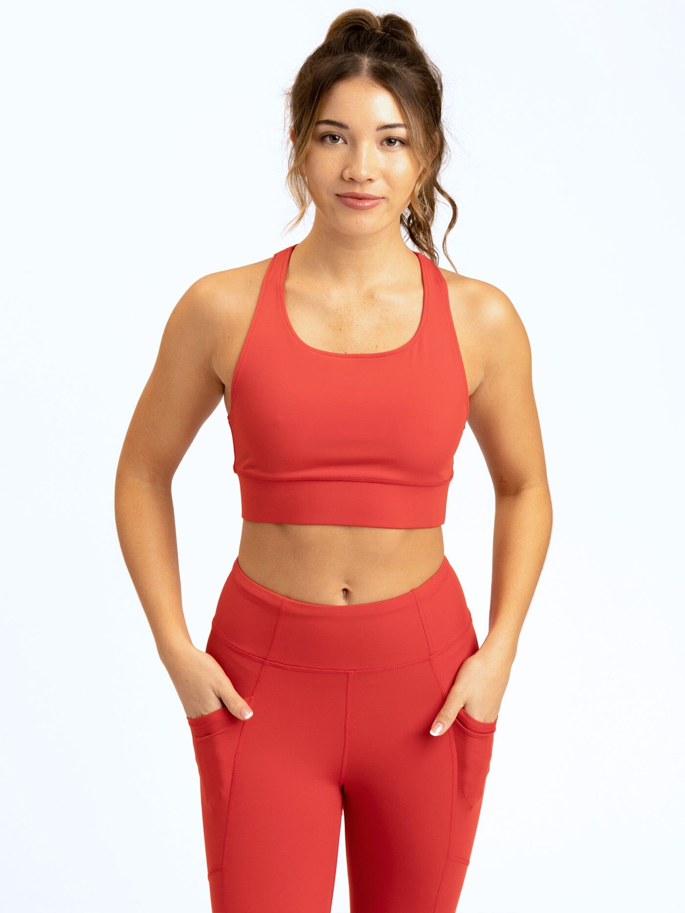 A woman wearing a vibrant red, fitted strappy sports bra with a scoop neckline and cropped length.