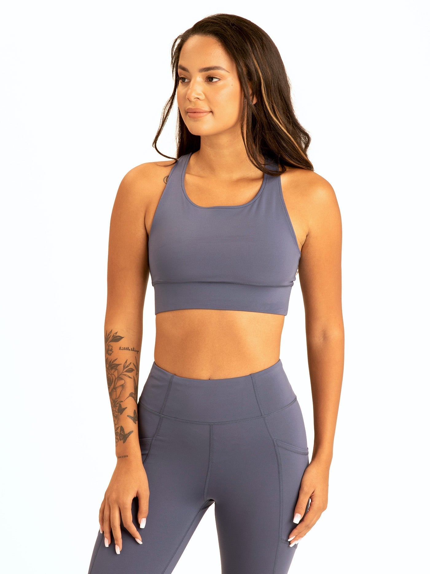 Back view of a woman wearing a minimalist Slate Blue strappy sports bra with a circular logo on the band.