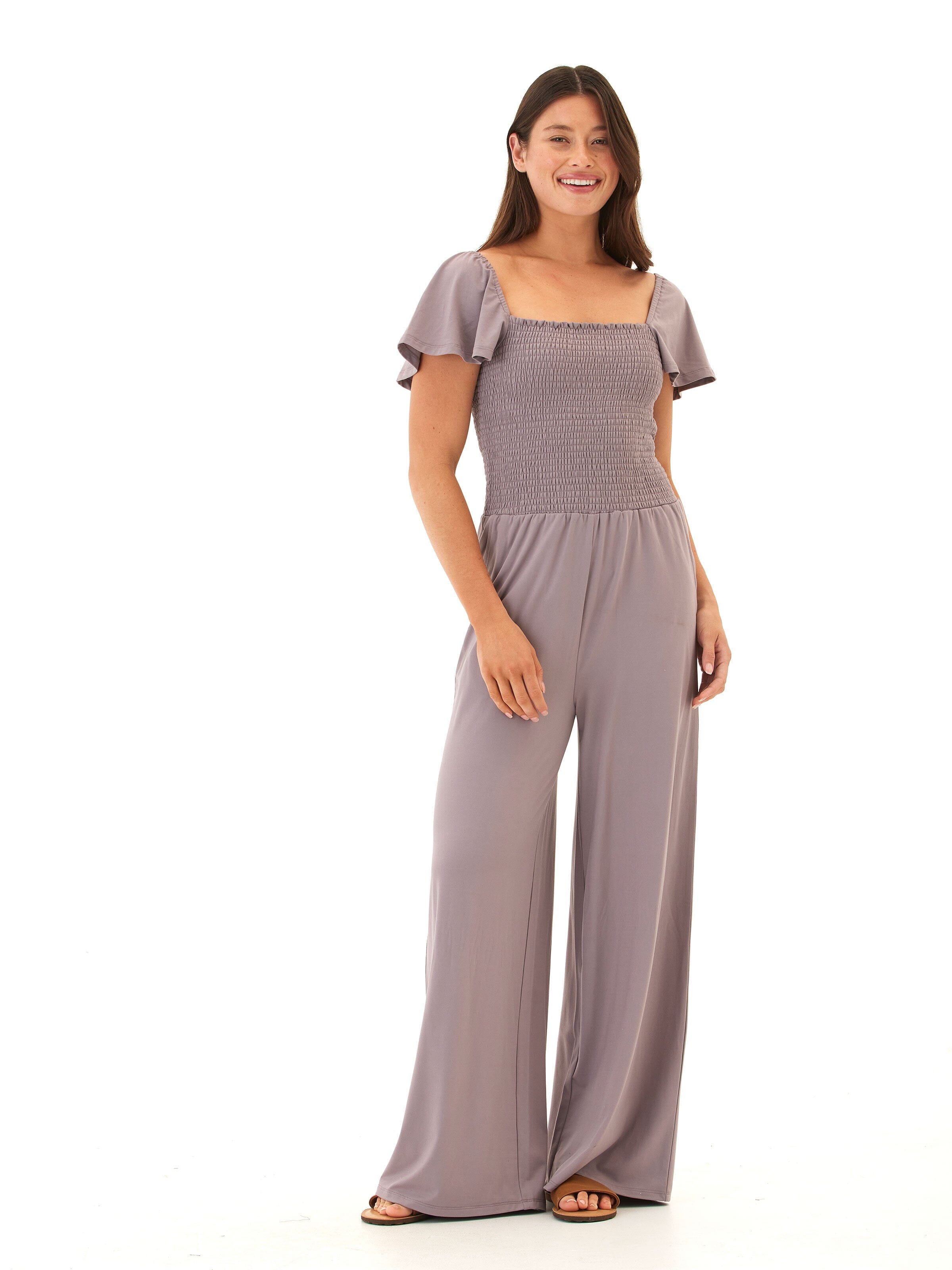 A woman wearing a dusty purple, wide-leg Luxe Jersey jumpsuit with a square neckline and flutter sleeves.