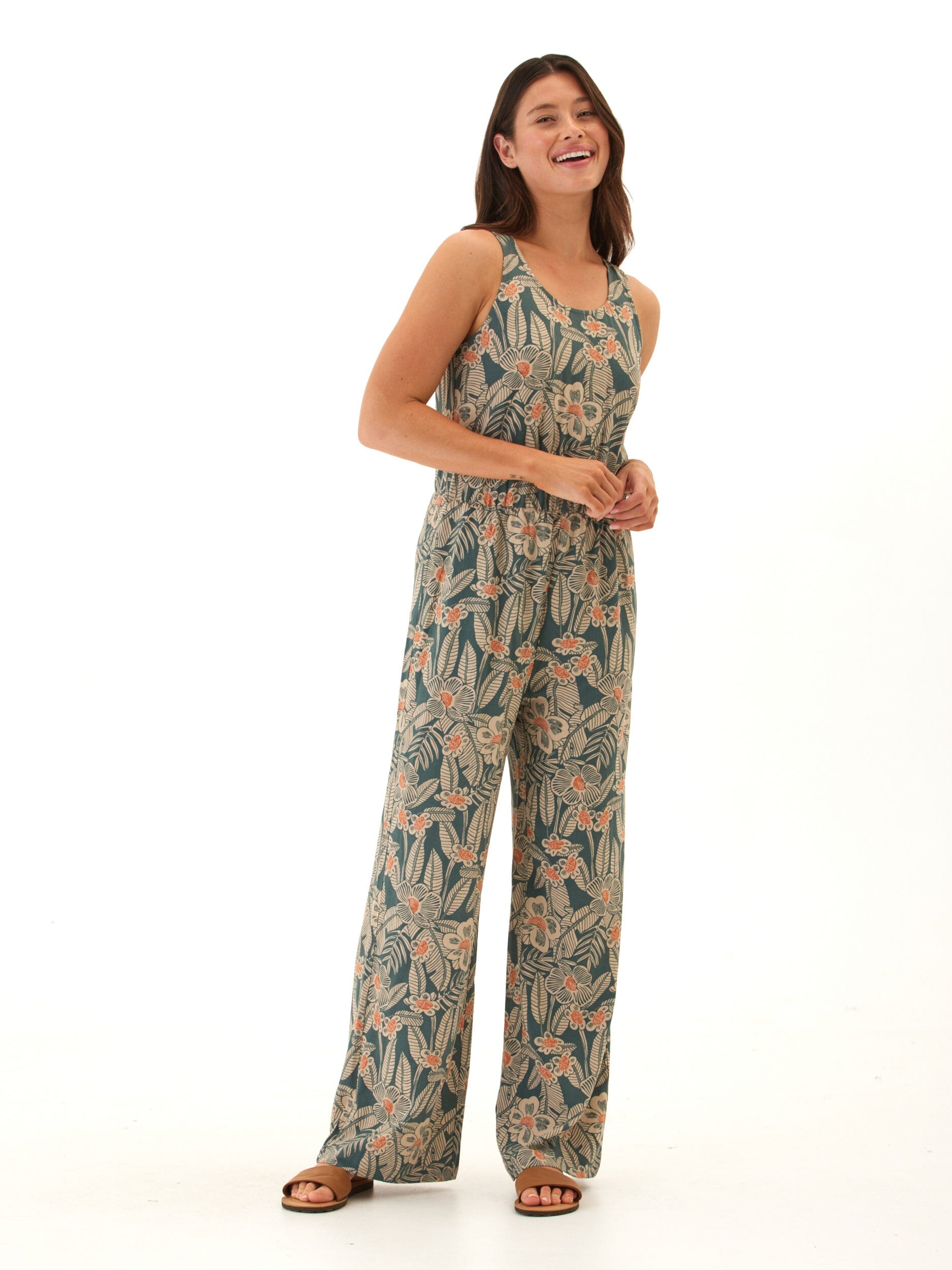 Woman wearing a sleeveless teal and peach floral print wide-leg jumpsuit with scoop neckline and elastic waist.