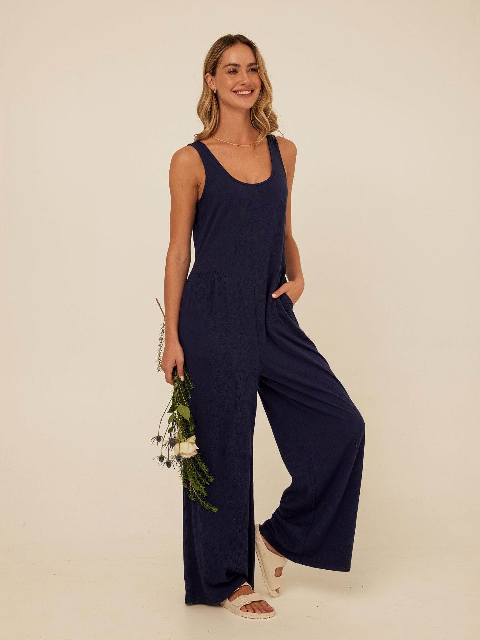 Woman wearing a navy blue sleeveless knit wide-leg jumpsuit with a scoop neckline and side pockets.