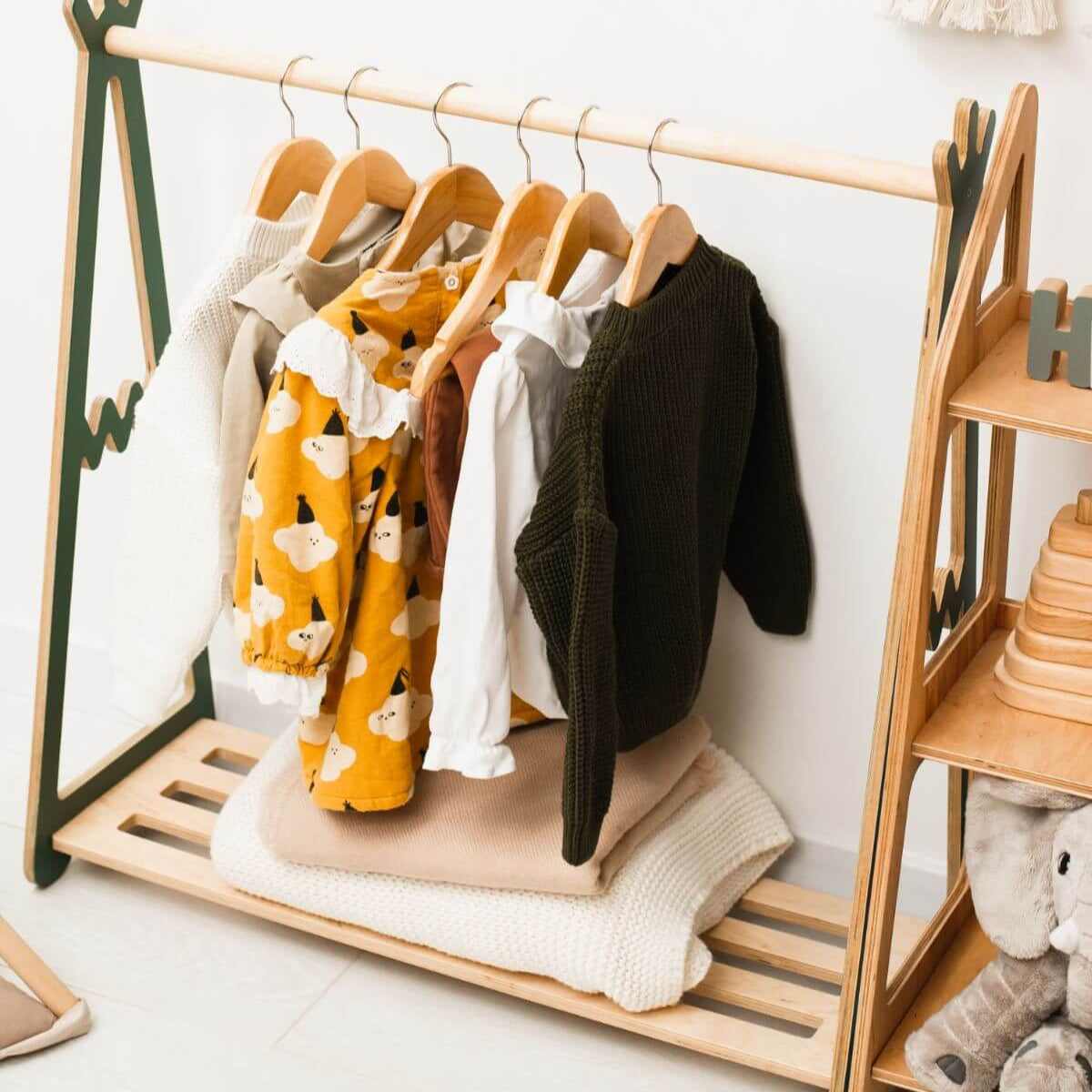 Teepee-shaped wooden clothing rack for kids' clothes in a nursery